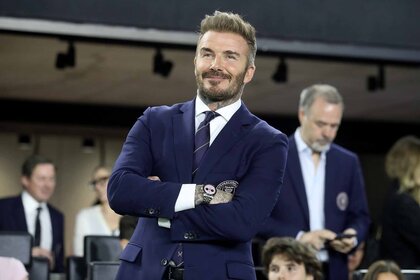 David Beckham smiles and folds his arms in a blue suit.
